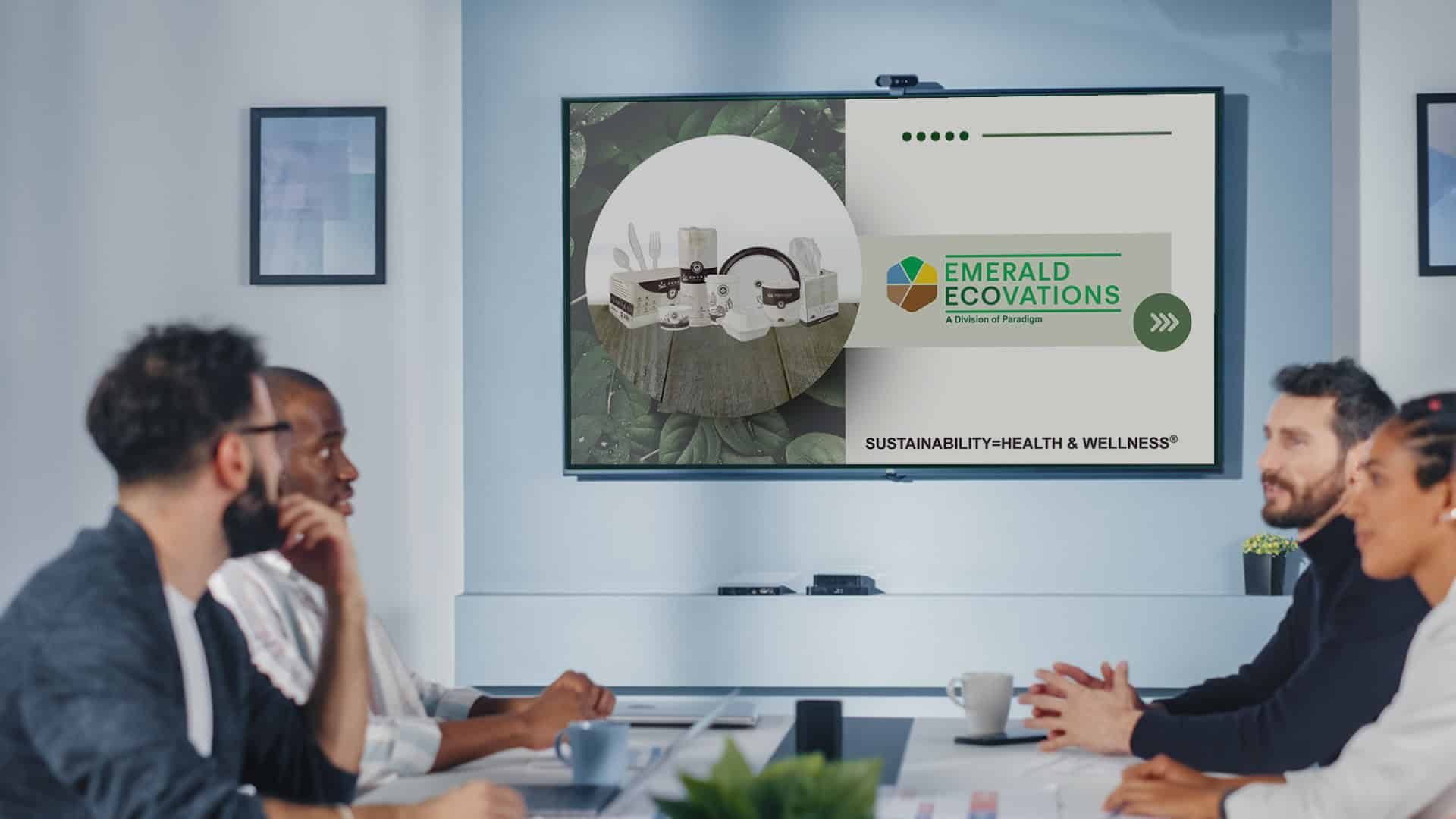 Four people in a meeting room attentively watch a presentation on a screen. The slide displays images of smart home devices and the logo "Emerald Ecovations," with the text "Sustainability = Health & Wellness" over a leafy background.